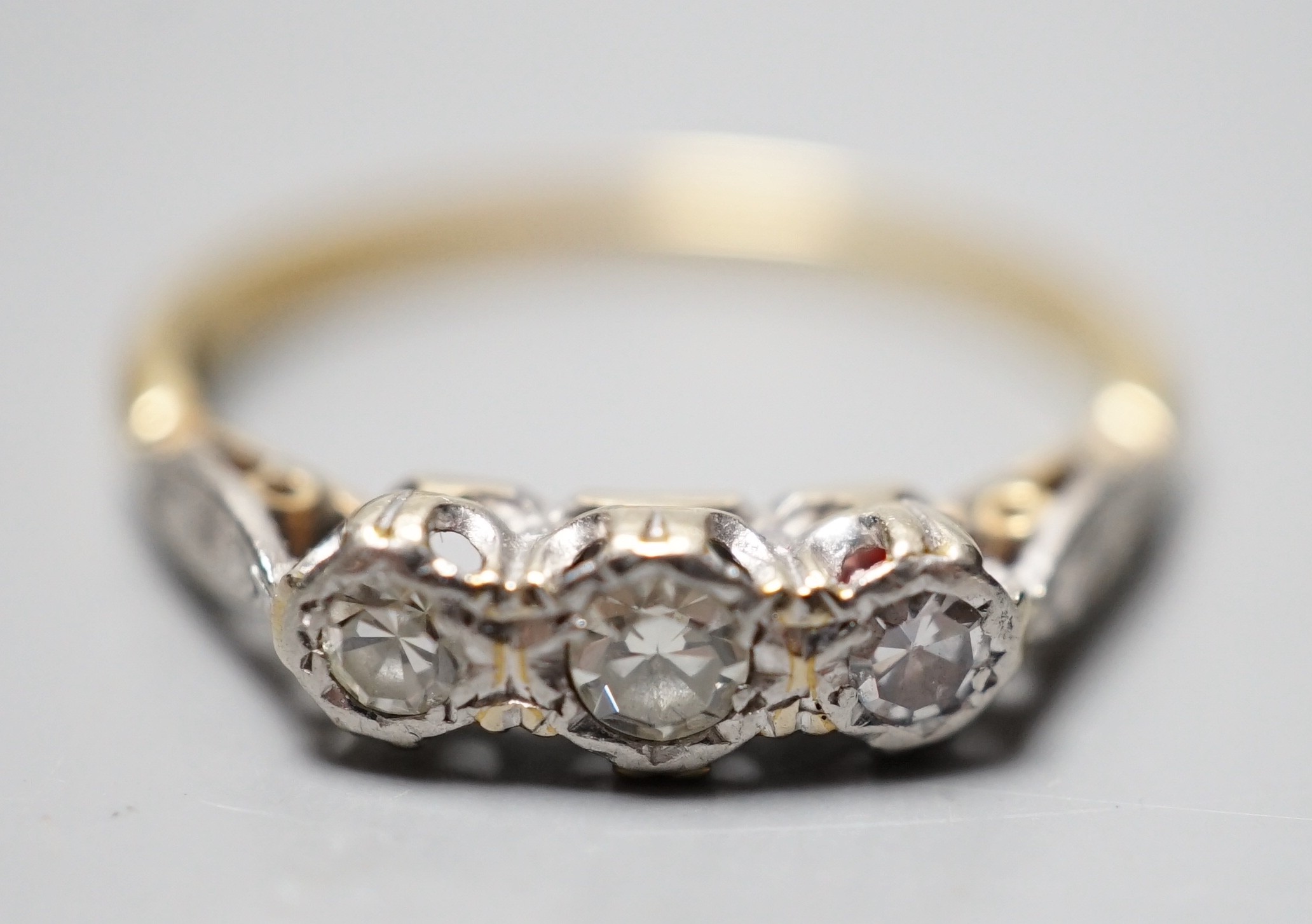 A yellow metal and illusion set three stone diamond ring, size O, gross weight 2.4 grams.